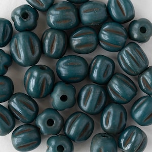 May include: A collection of teal-colored beads with brown grooves and various shapes. Some beads are round, others are oblong, and some have a flower-like shape. The beads are likely for jewelry making or crafting.
