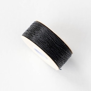 Könnte beinhalten: Eine Rolle schwarzes Garn, eng um einen Pappkern gewickelt. Das Garn scheint aus einer Naturfaser zu bestehen, und die Rolle ist vor einem weißen Hintergrund platziert. Ideal zum Basteln und Verpacken.