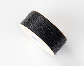 Puede incluir: Un carrete de hilo negro, enrollado firmemente alrededor de un núcleo de cartón. El hilo parece estar hecho de una fibra natural, y el carrete está sobre un fondo blanco. Ideal para manualidades y embalaje.