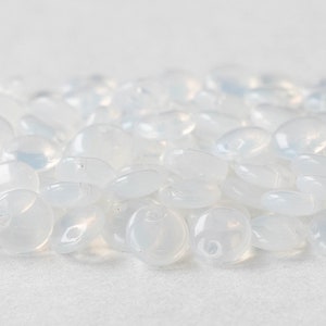 May include: A pile of translucent white glass beads, each bead is slightly oval shaped.