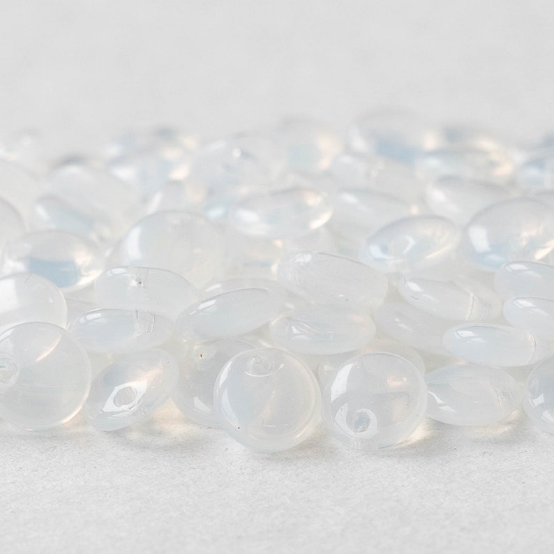 May include: A pile of translucent white glass beads, each bead is slightly oval shaped.