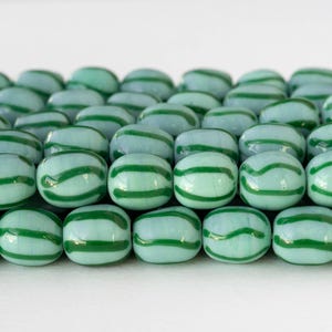 Può includere: Primo piano di numerosi biglie di vetro blu chiaro, ognuna ornata da strisce curve verde scuro. Le biglie sono fittamente raggruppate, formando un motivo ripetitivo. L'immagine mostra una collezione di oggetti decorativi in vetro.