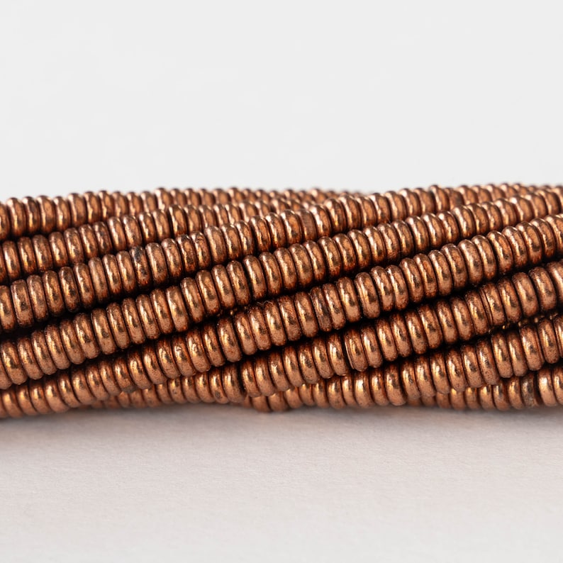 May include: A close-up of a strand of copper-colored beads. The beads are round and have a smooth, shiny finish.