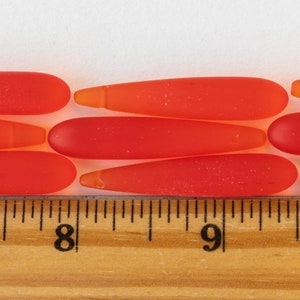 Puede incluir: Primer plano de una fila de cuentas de vidrio naranja y rojo, con una regla que muestra una medida de 20,3 cm.
