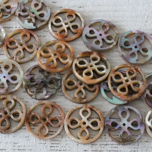May include: A collection of round, iridescent, mother-of-pearl shell beads with a carved, intricate, floral design. The beads are a light brown color with hints of pink and green.