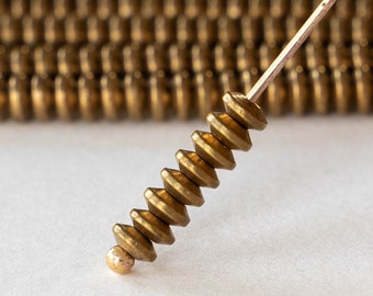 May include: A gold-colored metal bead with a unique, faceted design. The bead is strung on a thin wire and is part of a larger strand of beads.