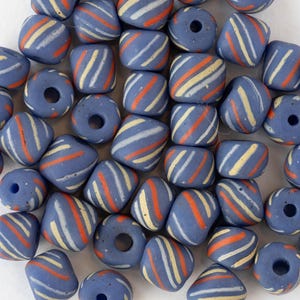 May include: A collection of blue beads with diagonal stripes in orange, white, and yellow. The beads are various shapes, including round and square, and have holes for stringing.