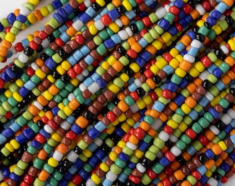 May include: Close-up of colorful seed beads in various colors, including red, yellow, blue, green, and brown. The beads are strung together, creating a textured and vibrant pattern. These beads are perfect for jewelry making and craft projects.