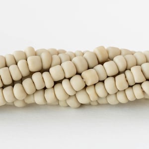 Könnte beinhalten: Nahaufnahme eines Abschnitts von getrocknetem Maiskolben. Die Körner sind hell, cremefarben und in ordentlichen Reihen angeordnet. Das Bild ist vor einem schlichten weißen Hintergrund aufgenommen, der die Textur und Form des Mais hervorhebt.