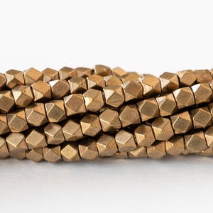 May include: Close-up of several strands of metallic gold-colored beads. The beads are geometric, with multiple facets creating a textured appearance. The beads are strung together, suggesting their use in jewelry or craft projects.