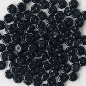May include: A large pile of black glass beads. The beads are round and have a hole in the center. They are perfect for jewelry making or other craft projects.