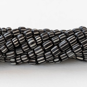 May include: Black and white striped glass beads. The beads are square shaped and have a glossy finish.