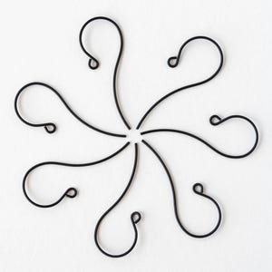 May include: A top-down view of a symmetrical arrangement of eight black metal hooks, each with a looped end. The hooks radiate from a central point, creating a floral or star-like pattern against a white background. The design is simple and elegant.