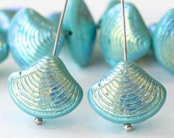 May include: A close-up of iridescent blue glass beads shaped like seashells. The beads have a textured surface and are strung on silver wires.