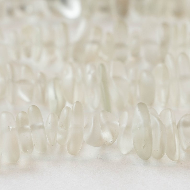 Pu&ograve; includere: Una collana di perline di vetro di mare bianco, ogni perla ha una forma unica e irregolare.