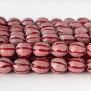 Può includere: Primo piano di una collezione di perline rosa rotonde con finitura lucida. Ogni perlina presenta due audaci strisce rosse orizzontali. Le perline sono disposte molto vicine tra loro, creando una superficie strutturata.