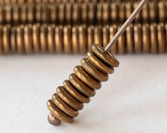 May include: A stack of gold-colored metal rings, each with a slightly different diameter, are strung together on a thin wire. The rings are stacked in a spiral shape, creating a unique and decorative piece.