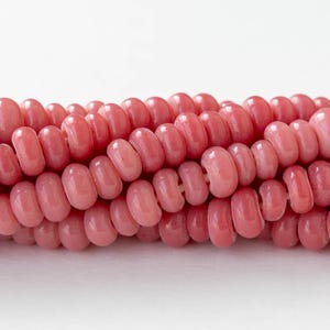 以下が含まれることがあります： ピンク色のガラスビーズの糸。各ビーズは丸く、中央に穴が開いています。ビーズは一列に並べられており、穴は視聴者の方を向いています。