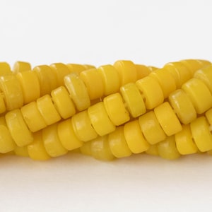 May include: Close-up of a strand of yellow beads. The beads are cylindrical with rounded edges and a hole running through the center. The beads are a bright, solid yellow color and are strung together in a spiral.