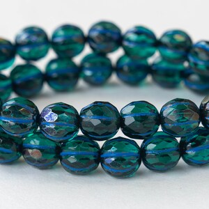 May include: A strand of dark green glass beads with blue stripes. The beads are faceted and have a slightly iridescent finish.