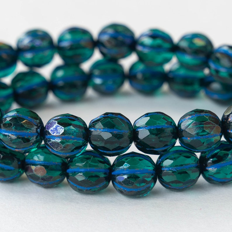 May include: A strand of dark green glass beads with blue stripes. The beads are faceted and have a slightly iridescent finish.