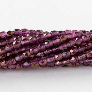 May include: A strand of purple glass beads with a copper metallic finish. The beads are faceted and have a slightly irregular shape.