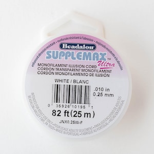 May include: White Supplemax Ultra monofilament illusion cord spool. The spool is labeled with the text "MONOFILAMENT ILLUSION CORD" and "WHITE / BLANC". The cord is .010 inches in diameter and 82 feet long.