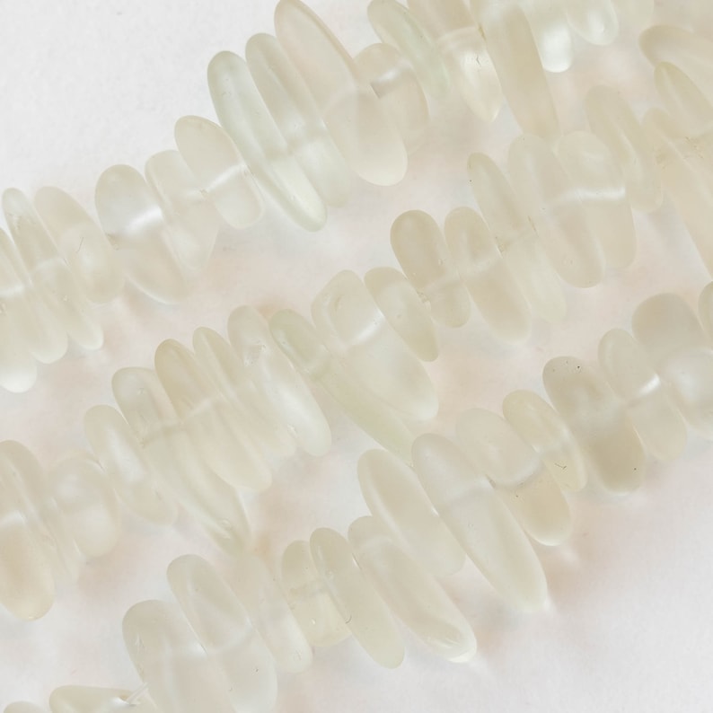 Pu&ograve; includere: Una collana di perline di vetro di mare bianco, ogni perla ha una forma unica e irregolare.