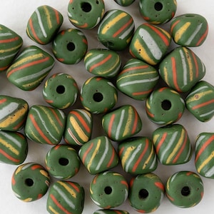 May include: A collection of green glass beads with diagonal stripes in white, orange, and yellow. The beads have a cylindrical or rounded square shape with a hole through the center, suitable for jewelry making or crafts.