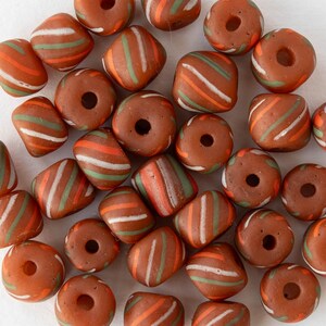 Peut inclure: Un assortiment de perles en verre marron, ornées de rayures orange, vertes et blanches. Les perles sont de formes variées, rondes et carrées, parfaites pour la création de bijoux ou les travaux manuels.