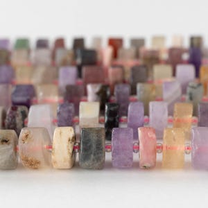 May include: Close-up of a strand of rectangular gemstone beads in various colors, including beige, purple, and pink. The beads are strung on a thin, pink cord, creating a colorful and textured pattern. The beads are approximately 0.5 inches in length.