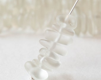 May include: A strand of frosted white glass beads, strung together on a silver wire. The beads are stacked in a graduated size, with the largest bead at the bottom and the smallest bead at the top.