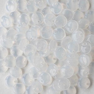 May include: A close-up view of a pile of translucent white round beads with a small hole in the center of each bead.