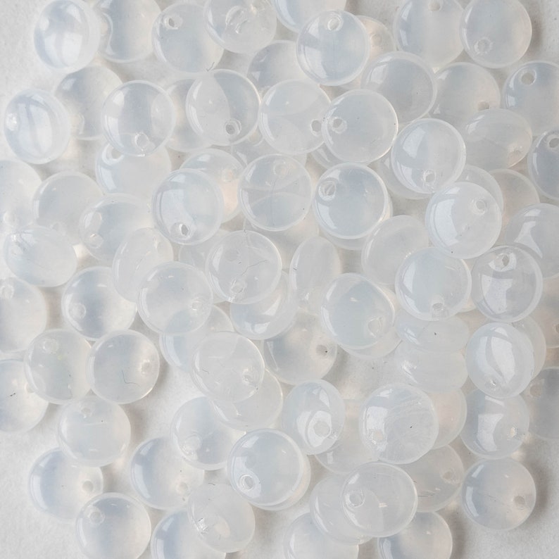 May include: A close-up view of a pile of translucent white round beads with a small hole in the center of each bead.