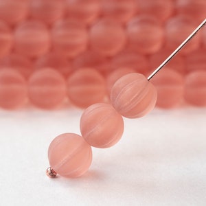 May include: Close-up of three peach-colored, round beads with etched lines, strung on a thin, copper-colored wire. The beads have a matte finish. A small copper-colored bead is at the end of the wire. More peach beads are blurred in the background.