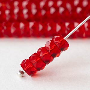 Puede incluir: Primer plano de una hebra de cuentas de vidrio facetadas rojas enhebradas en un alambre plateado. Las cuentas son pequeñas y tienen forma de estrella.