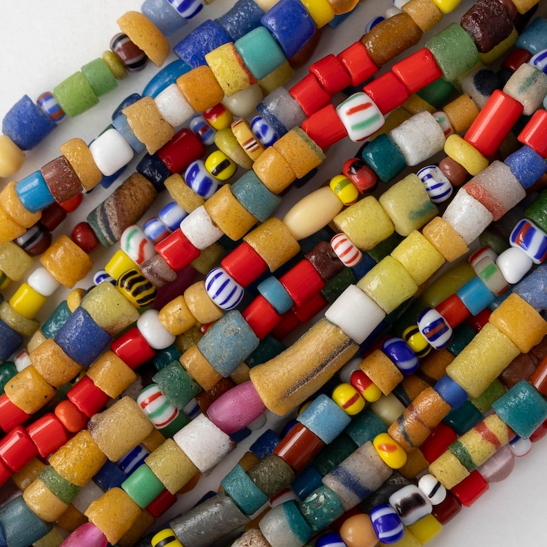 May include: Strands of colorful glass beads in various shapes and sizes. The beads are a mix of red, yellow, blue, green, and white, with some featuring striped or patterned designs. The beads are strung together, creating a vibrant and textured appearance.