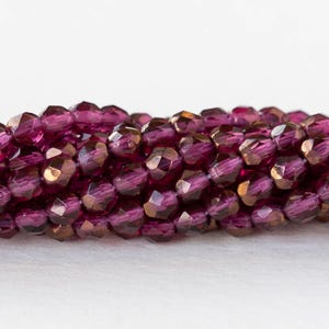 May include: A strand of iridescent purple glass beads with a faceted finish. The beads are small and round, and they have a metallic sheen.