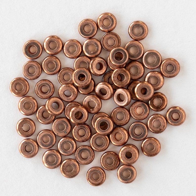 May include: A large pile of copper-colored metal beads. The beads are round with a hole in the center.