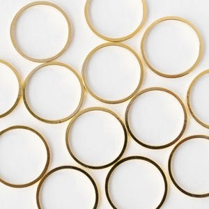 Op de afbeelding: Luchtfoto van meerdere goudkleurige metalen ringen gerangschikt op een witte ondergrond. De ringen zijn cirkelvormig met een dunne gouden band. De ringen zijn gelijkmatig verdeeld en creëren een patroon tegen de witte achtergrond.