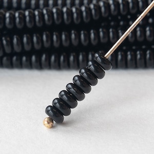 May include: A close-up of a black bead necklace with a gold bead at the end. The beads are round and have a slightly textured surface.