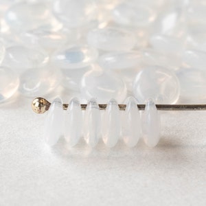 May include: A strand of white oval-shaped glass beads strung on a silver wire. The beads are translucent and have a slight iridescent sheen.