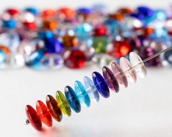 May include: A strand of colorful, disc-shaped glass beads in a rainbow of colors, including red, orange, yellow, green, blue, and purple. The beads are strung on a thin wire, with a blurred background of other colorful beads.