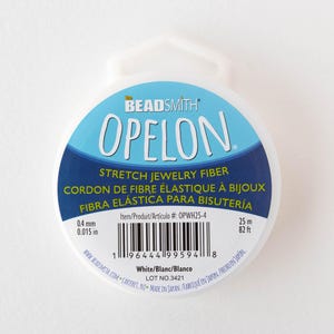 May include: White spool of OPELON stretch jewelry fiber. The label includes the text "STRETCH JEWELRY FIBER" and measurements of 0.4 mm and 0.015 in. The spool contains 82 ft of fiber.