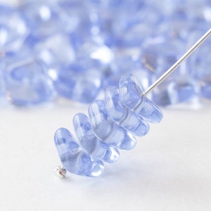 May include: A close-up of a strand of light blue glass beads strung on a silver wire. The beads are shaped like teardrops and are arranged in a spiral pattern.