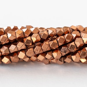 May include: A strand of copper-colored faceted beads. The beads are small and have a geometric shape.