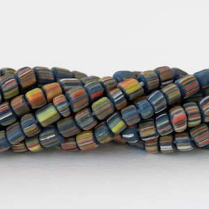 May include: Close-up of a strand of colorful, cylindrical beads. The beads are primarily blue, with stripes of orange, yellow, white, and brown. The beads are strung together, creating a textured and vibrant pattern. The beads are likely used for jewelry making.