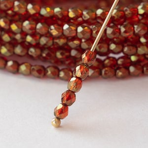 May include: A close-up of a strand of red iridescent glass beads strung on a thin wire. The beads are faceted and have a metallic sheen.