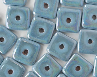 May include: A group of light blue square ceramic beads with a hole in the center. The beads have an iridescent finish.