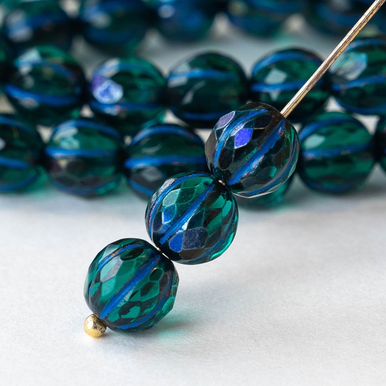 May include: A strand of dark teal blue glass beads with a faceted, striped design. The beads are strung on a silver wire.